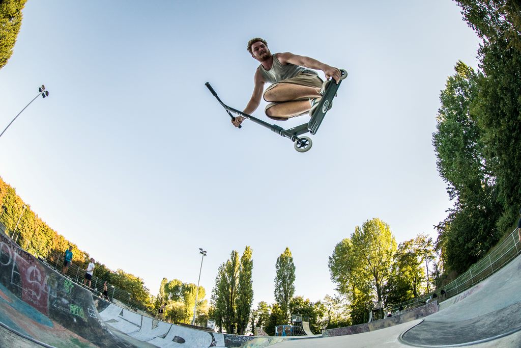 Homme faisant un saut en trottinette freestyle dans skatepark