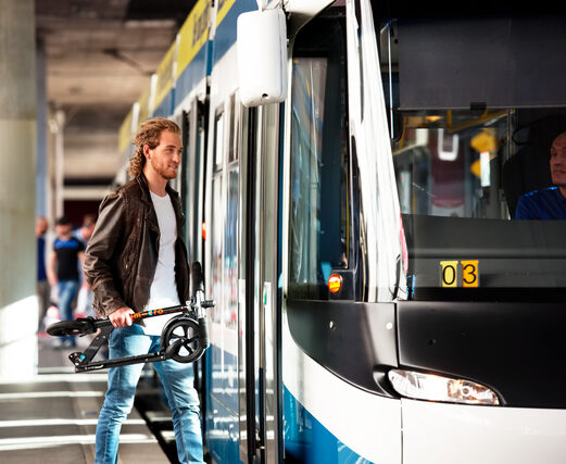 homme tenant une trottinette micro pliée à la main entre dans un transport en commun