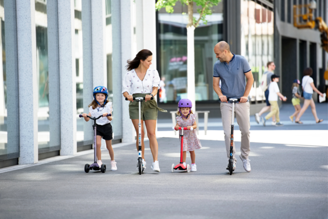 une famille en trottinette en ville, chacun a sa propre trottinette adaptée à sa taille