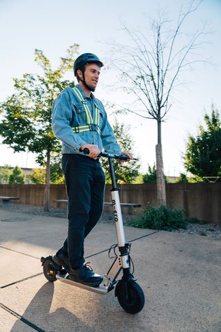 homme habillé en tenue de ville sur une trottinette électrique micro portant un casque et un gilet réfléchissant